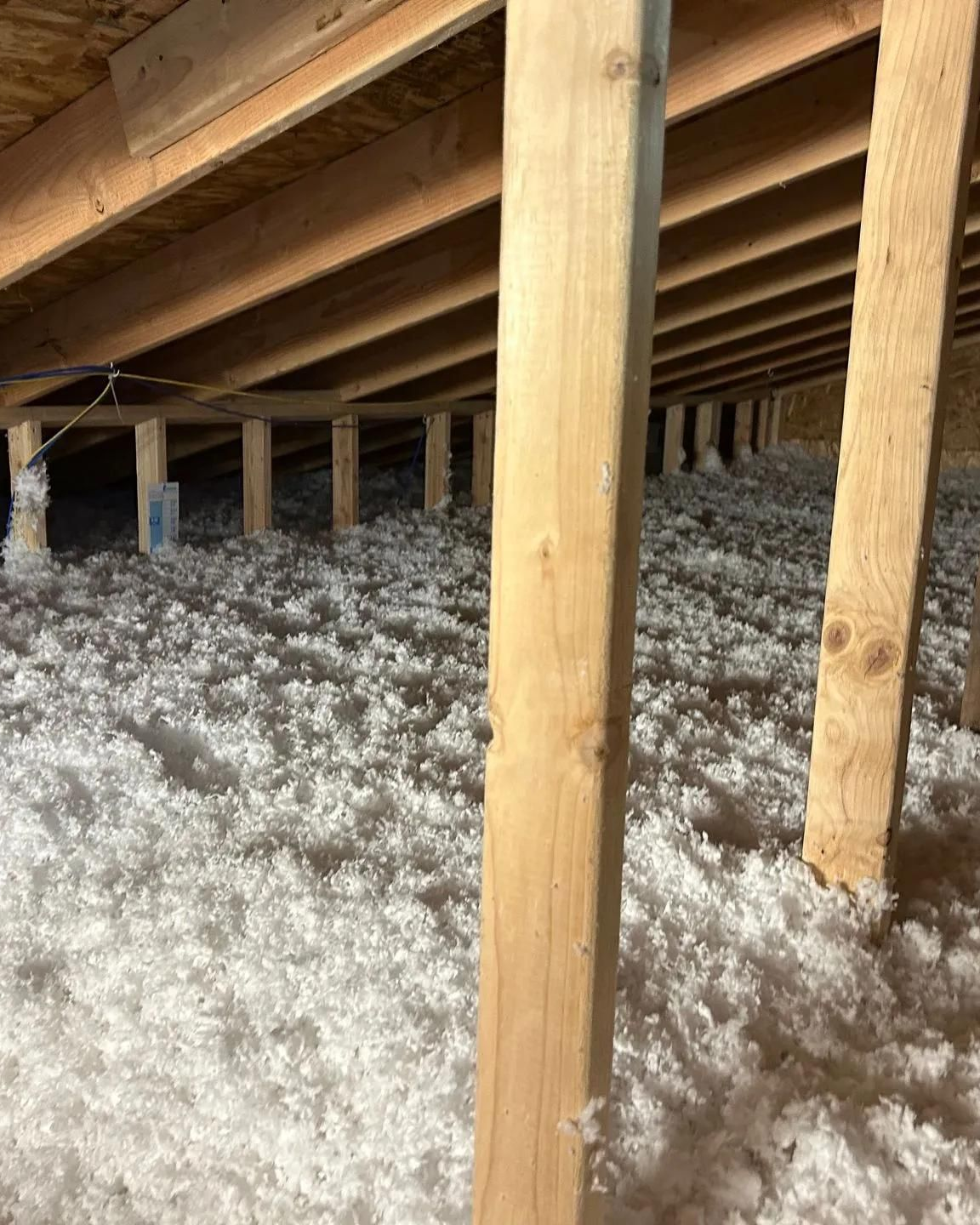 Insulated attic with wooden beams and joists above a thick layer of white insulation