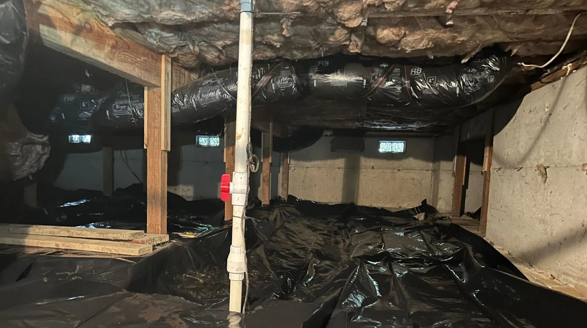 Crawlspace with exposed pipes, black plastic vapor barrier, and insulated ceiling joists.