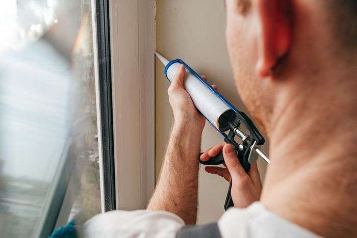 Person using a caulking gun to seal around a window frame.