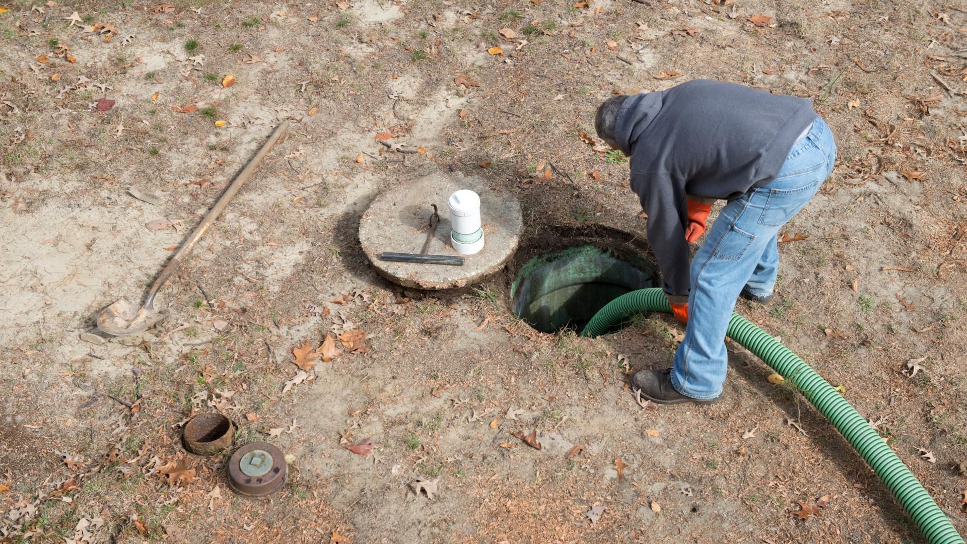 Man using a hose to pump out a septic tank in a yard.