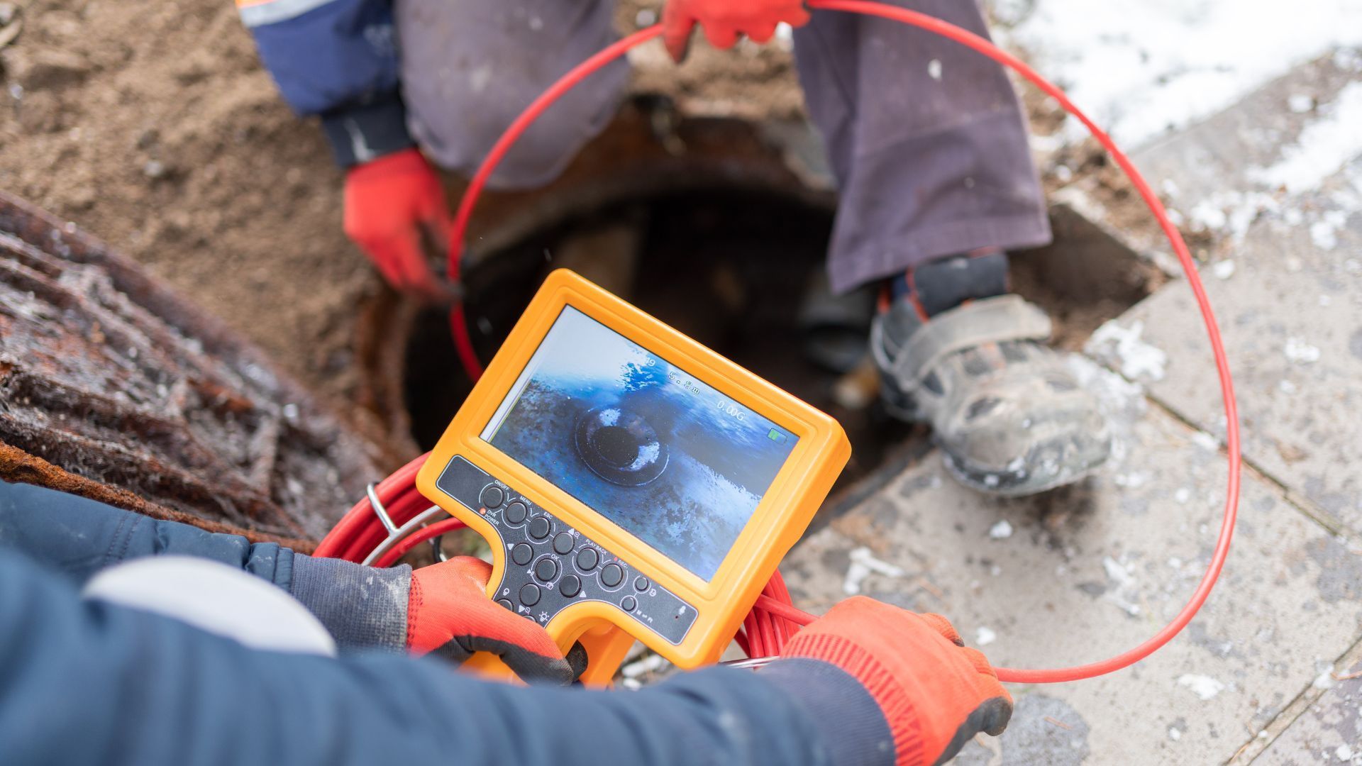 Worker using a yellow inspection camera to view inside a hole in the ground