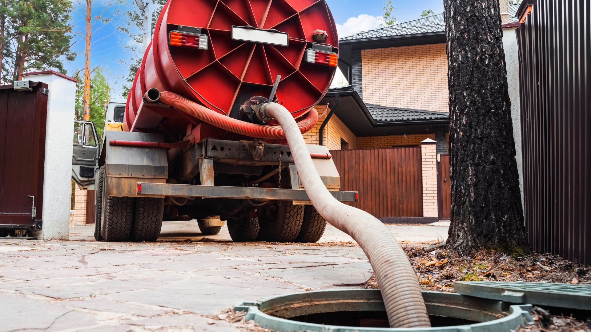 Red vacuum hose connected to a truck, clearing debris from a manhole in a driveway