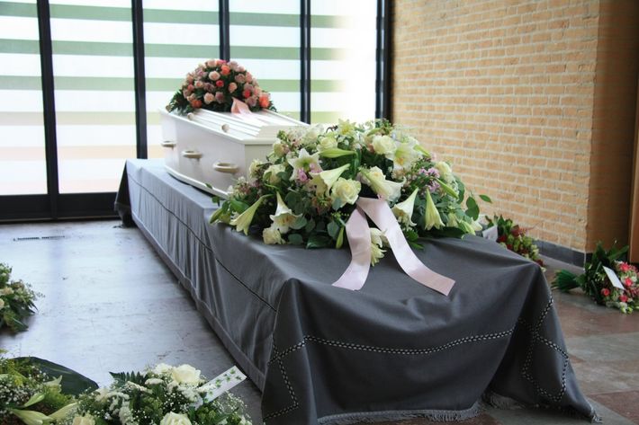Bara bianca con composizioni floreali su un tavolo drappeggiato di nero in una camera ardente.