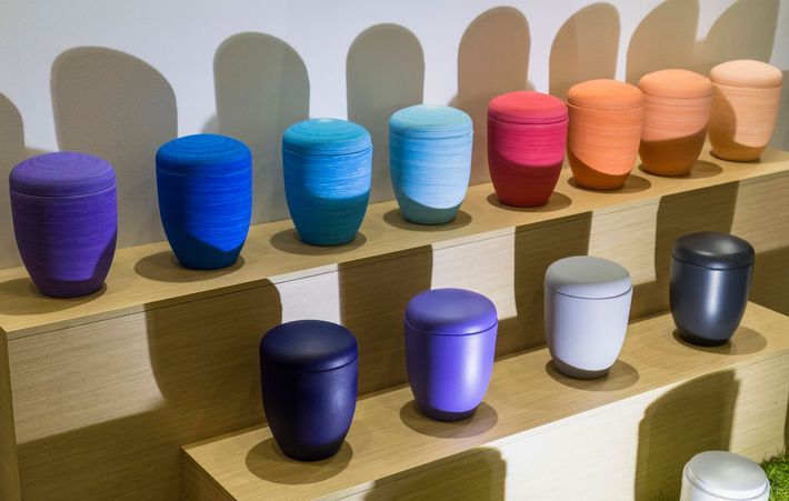 Tazze in ceramica colorate, disposte su ripiani a gradini, con smalti viola, blu, rosa, pesca e grigi.