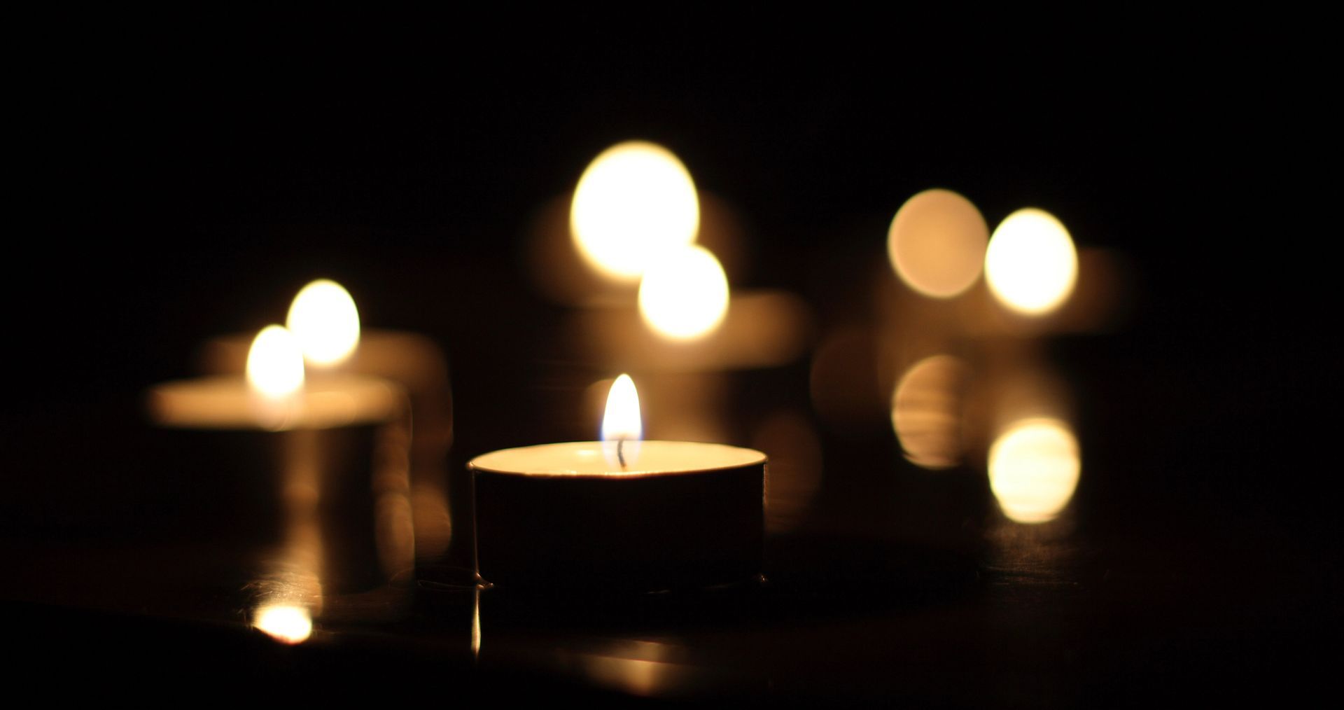 Candele accese che brillano in una stanza buia, con un lumino in primo piano e luci sfocate sullo sfondo.