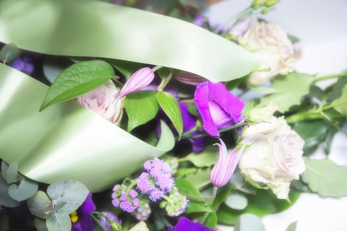 Bouquet floreale con fiori viola e bianchi avvolti da un nastro verde chiaro.
