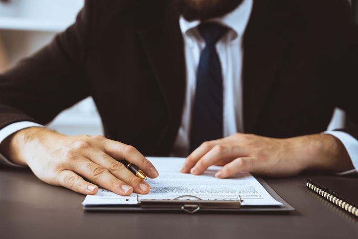 Mani che firmano un documento a una scrivania durante una riunione di lavoro.