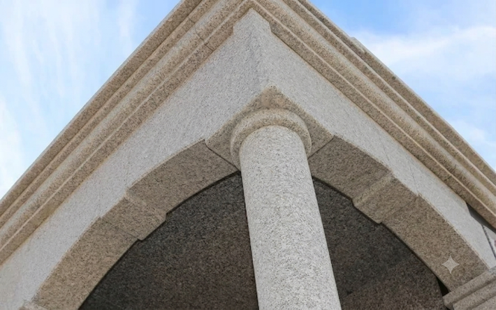 Primo piano di un angolo di un edificio con una colonna bianca e una copertura del tetto beige con finitura testurizzata, sullo sfondo del cielo.