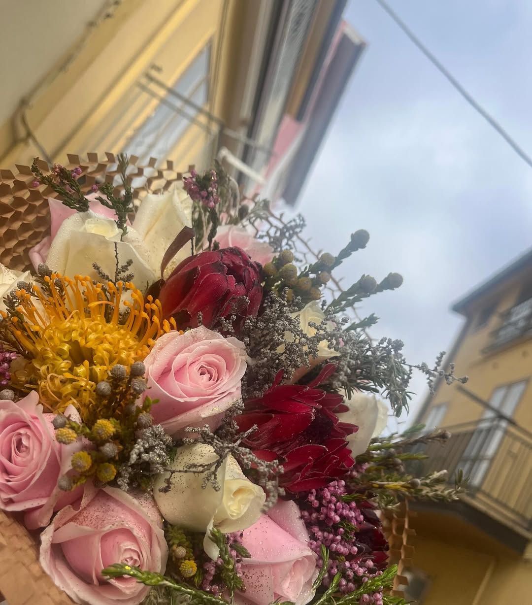 Bouquet di fiori rosa, bianchi e rossi sullo sfondo di un cielo tenue e dei balconi degli edifici.