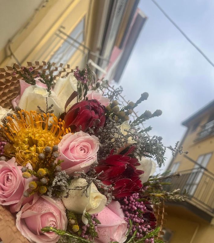 Bouquet di fiori rosa, rossi e bianchi con boccioli gialli sullo sfondo di una strada e di un edificio.