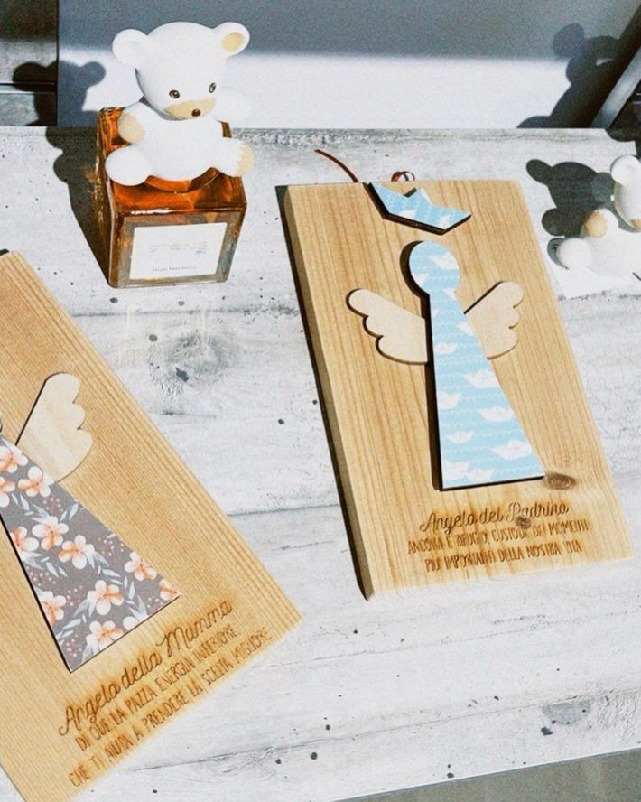 Su un tavolo bianco, etichette regalo a forma di angelo realizzate a mano, con un piccolo orsacchiotto in una scatola di legno nelle vicinanze.