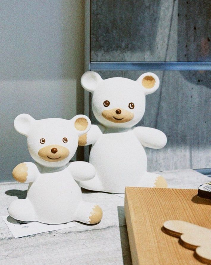Due statuette di orsetti di peluche bianchi con orecchie e zampe beige sono appoggiate su un tavolo vicino a una finestra.