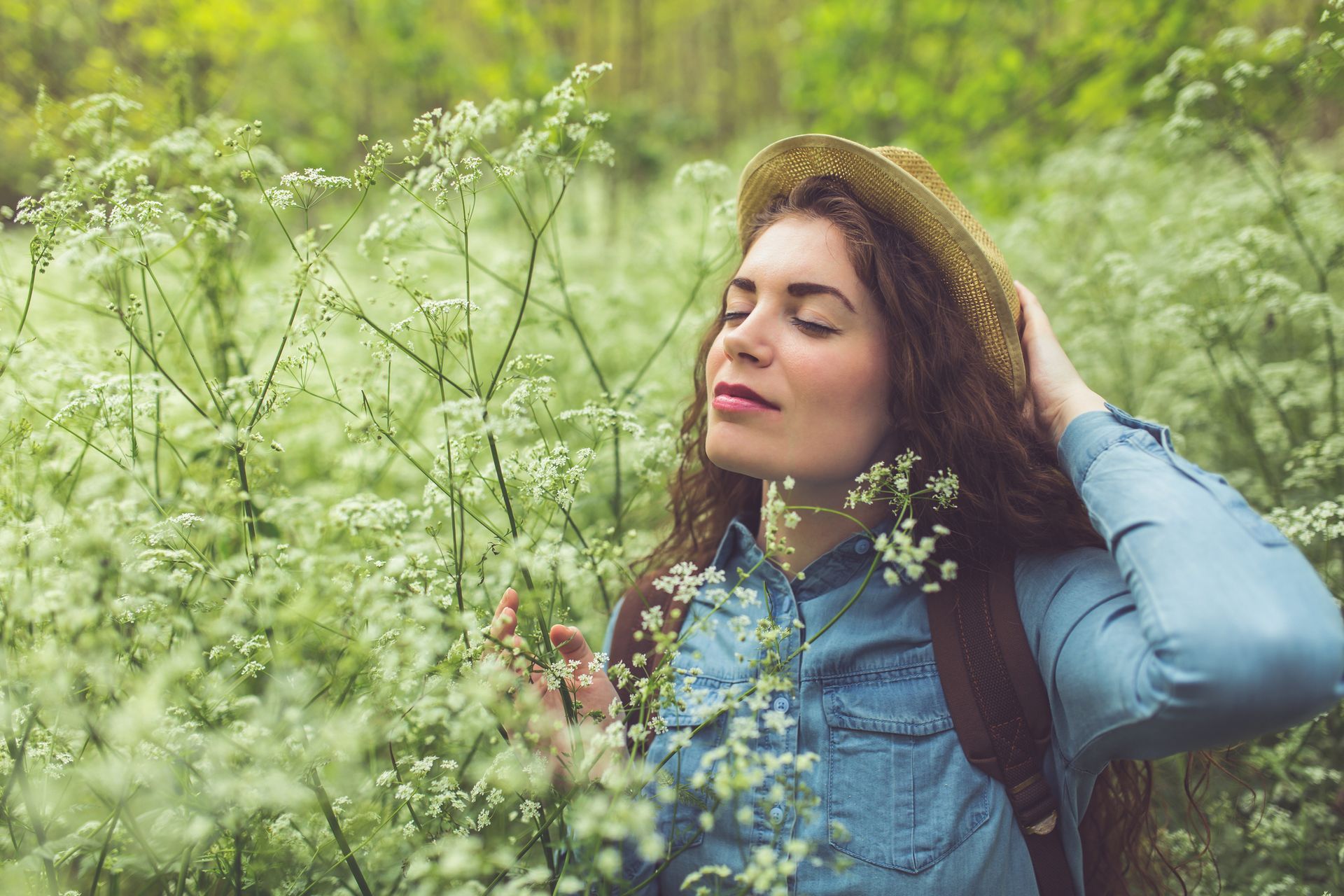 A woman in a straw hat is smelling flowers in a field.