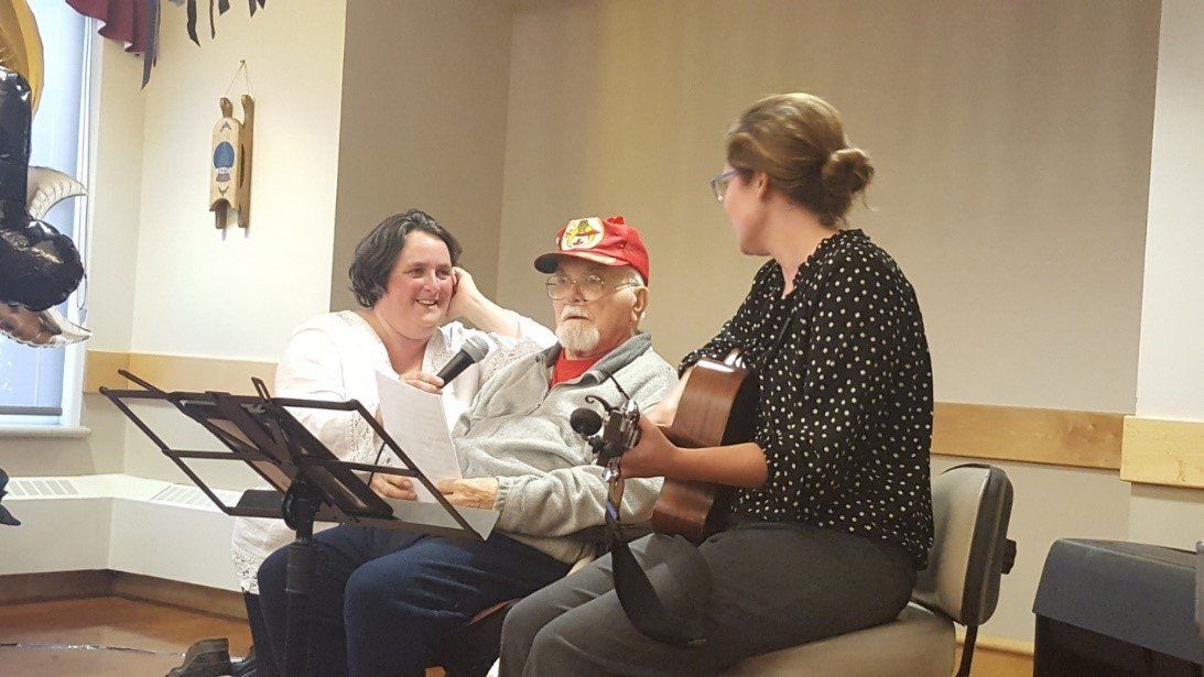 A group of people are sitting in chairs playing guitars and singing into microphones.