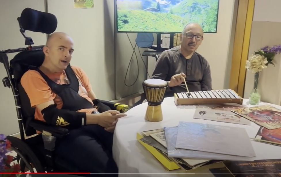 A man in a wheelchair is sitting at a table playing a drum