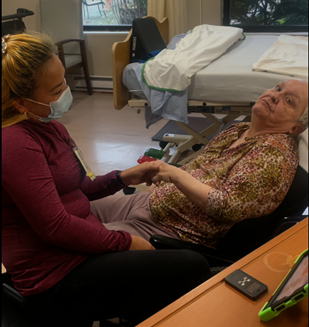 A woman wearing a mask sits next to an elderly woman in a wheelchair