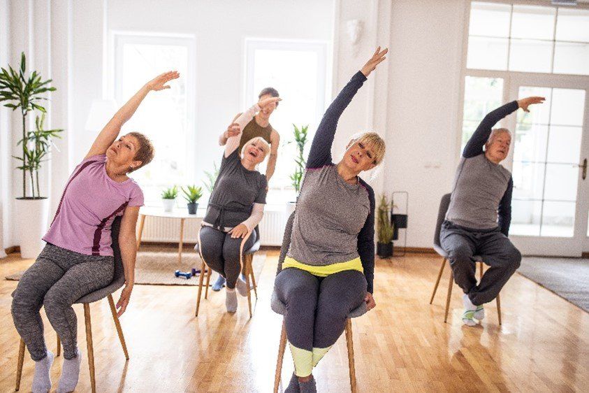 A group of older people are sitting in chairs doing stretching exercises.
