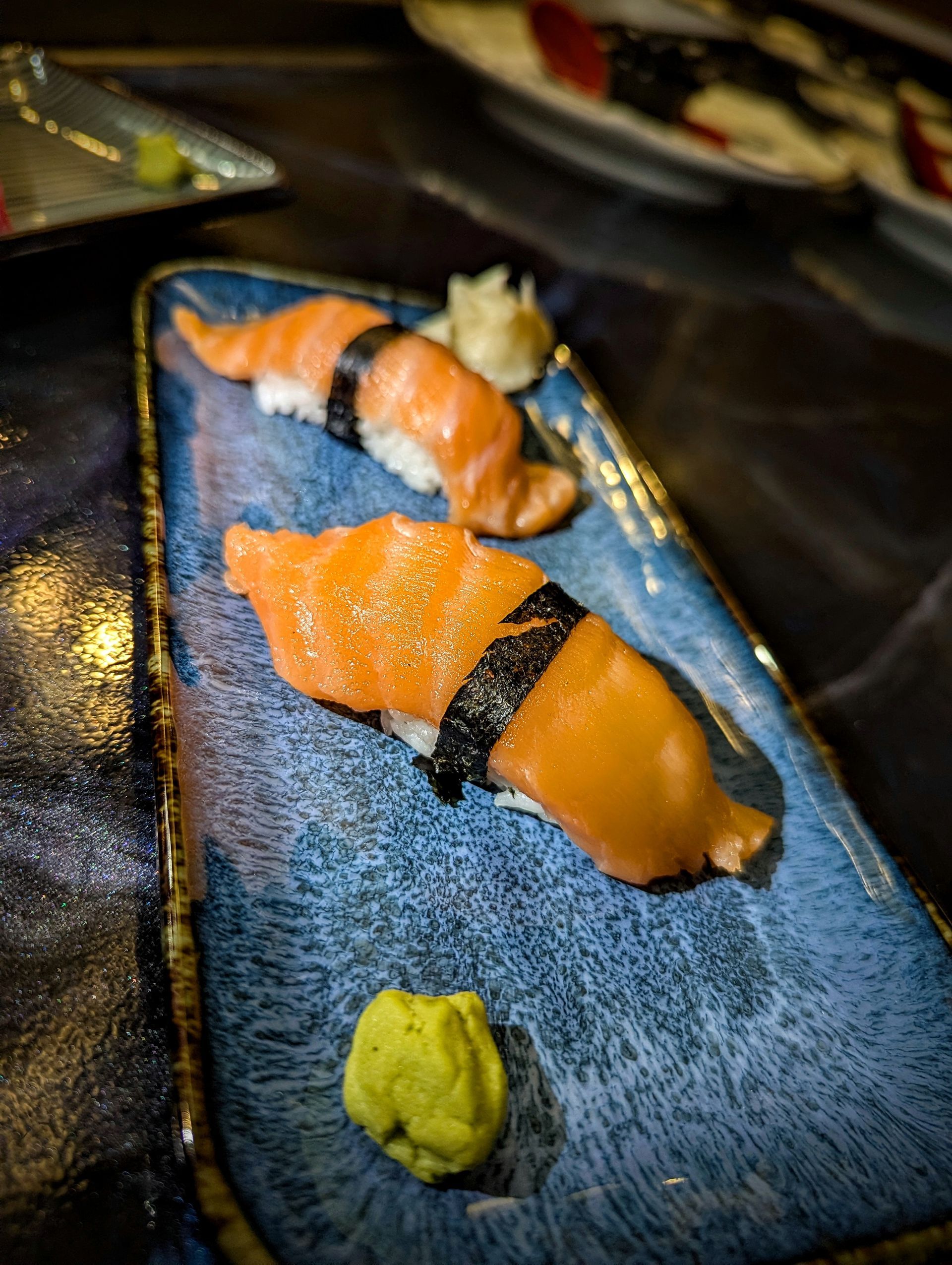Salmon sushi on a blue plate with wasabi in the foreground