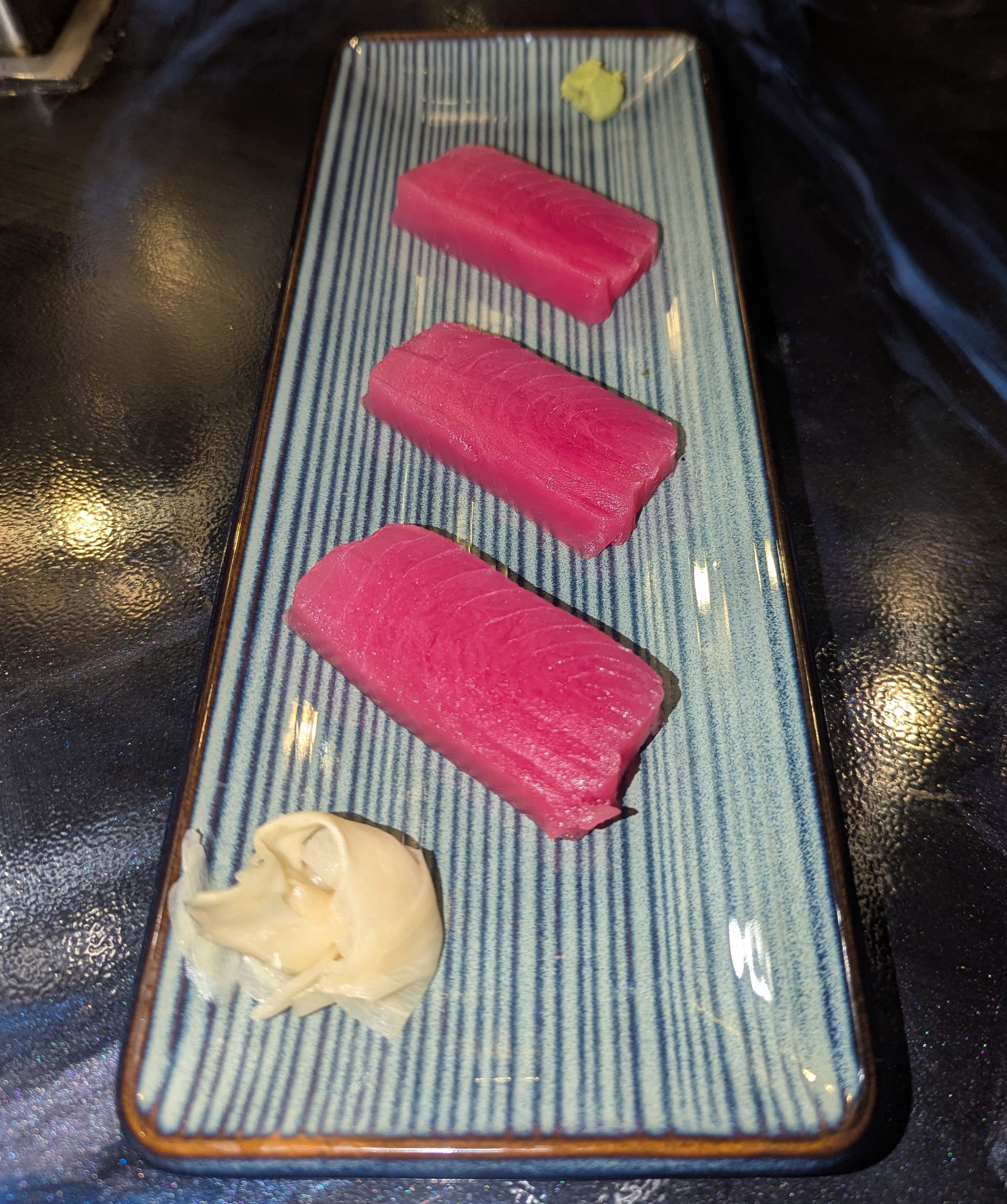 Three pink sushi pieces on a rectangular plate with a small dollop of ginger and wasabi