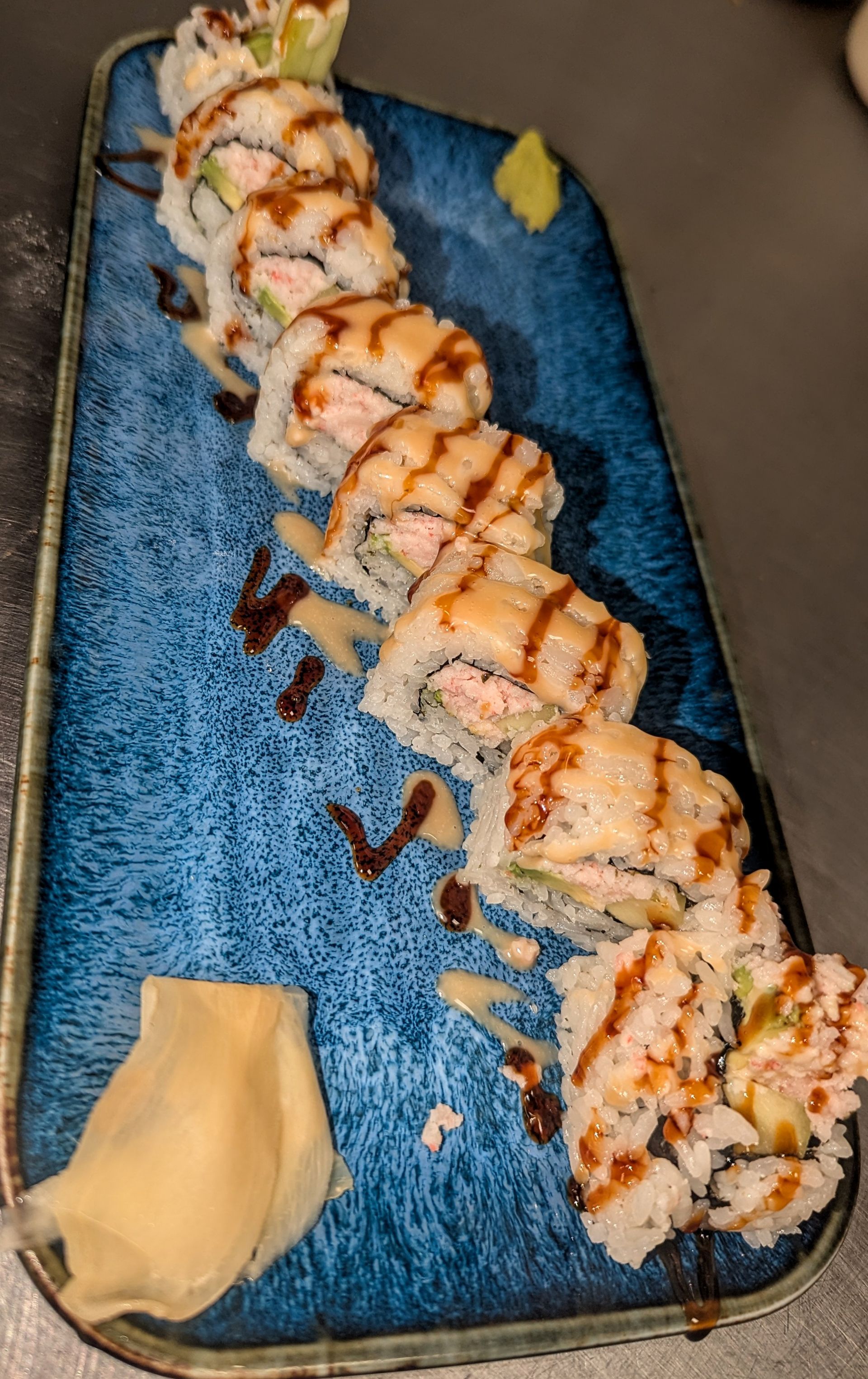 Sushi rolls on a blue plate, drizzled with sauce and topped with a lemon wedge.