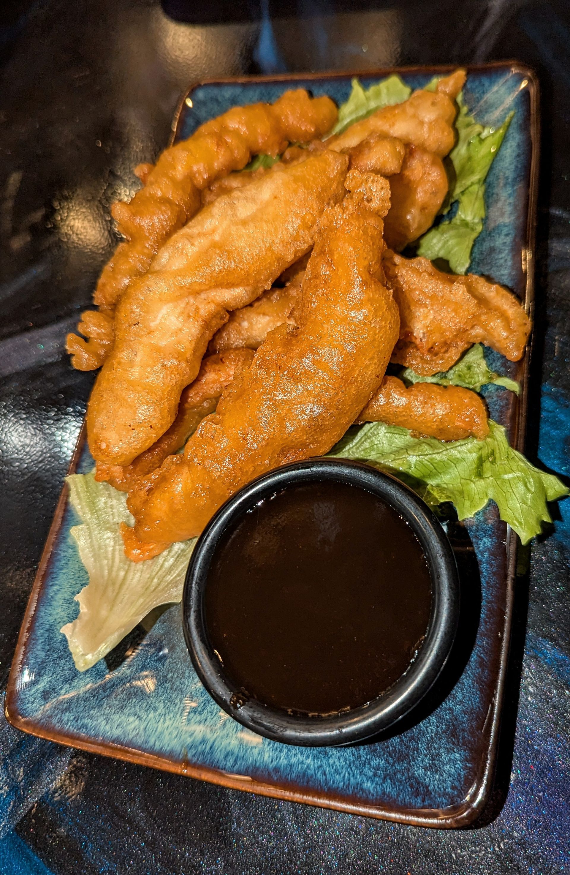 Fried chicken strips on a plate with lettuce and a cup of dark dipping sauce