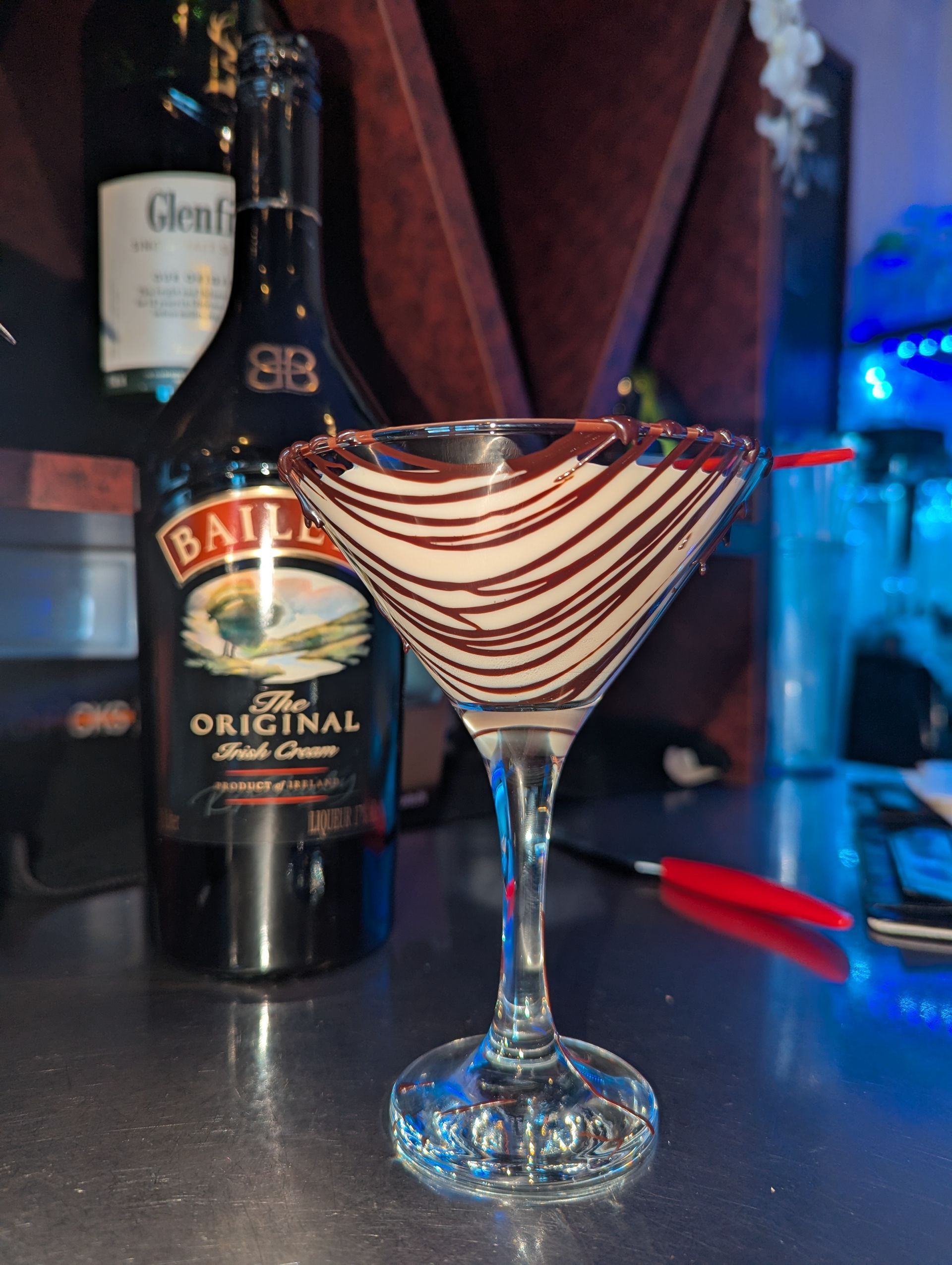 Chocolate-drizzled martini glass on a bar counter with bottles in the background