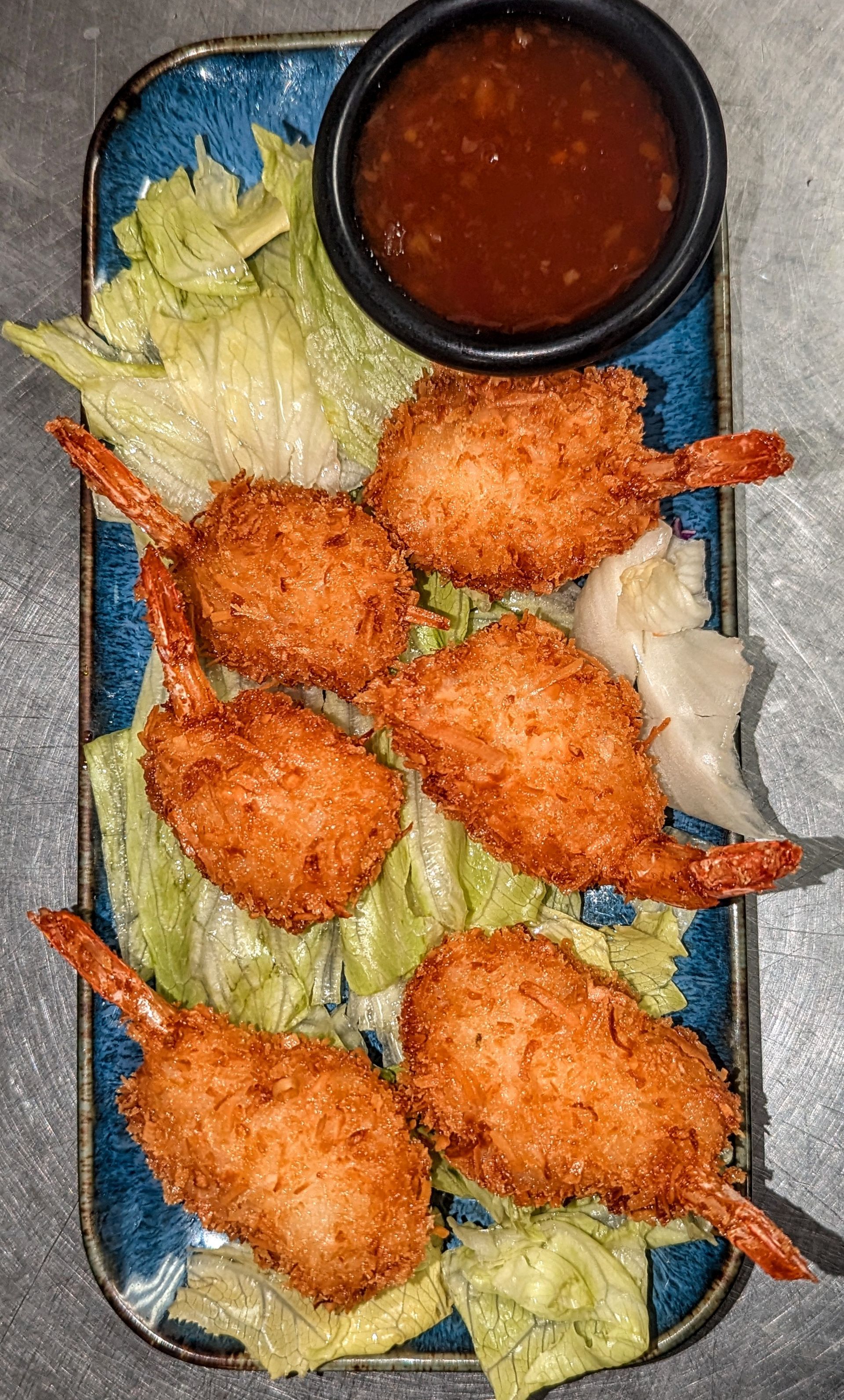 Breaded shrimp on lettuce in a tray with a small cup of red dipping sauce