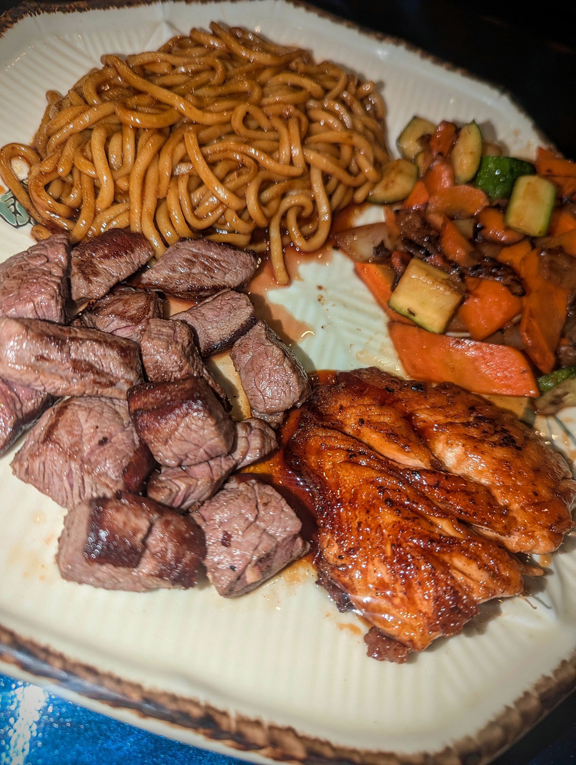 Plate with noodles, sliced beef, glazed chicken, and mixed vegetables on a decorative dish