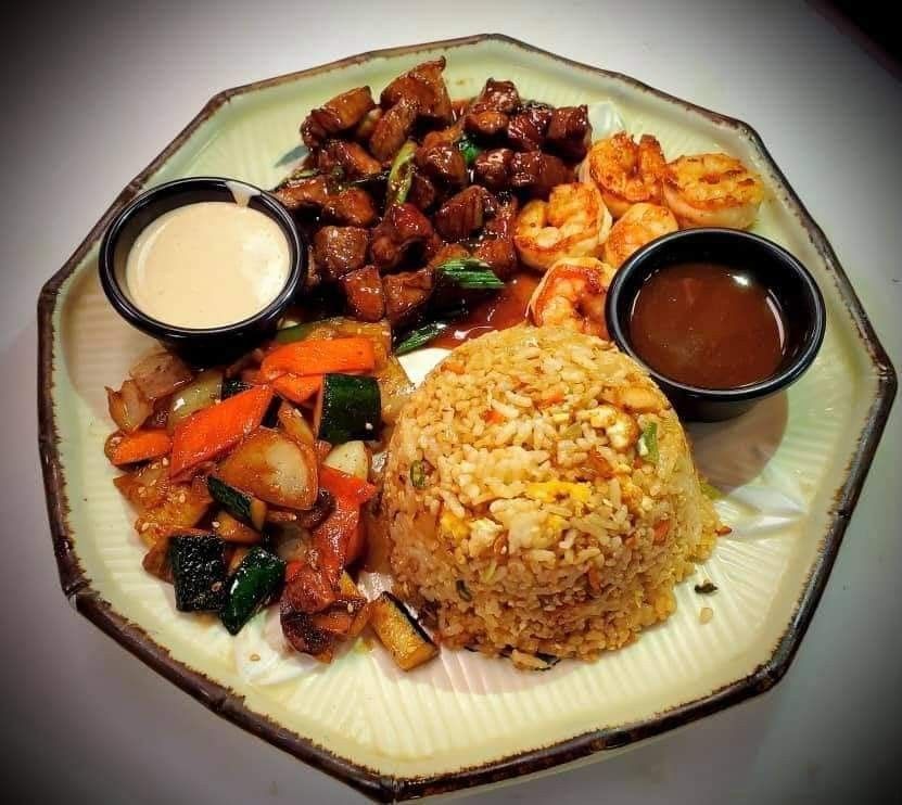 Plate of Chinese food with fried rice, stir-fried meat and vegetables, dumplings, and two dipping sauces