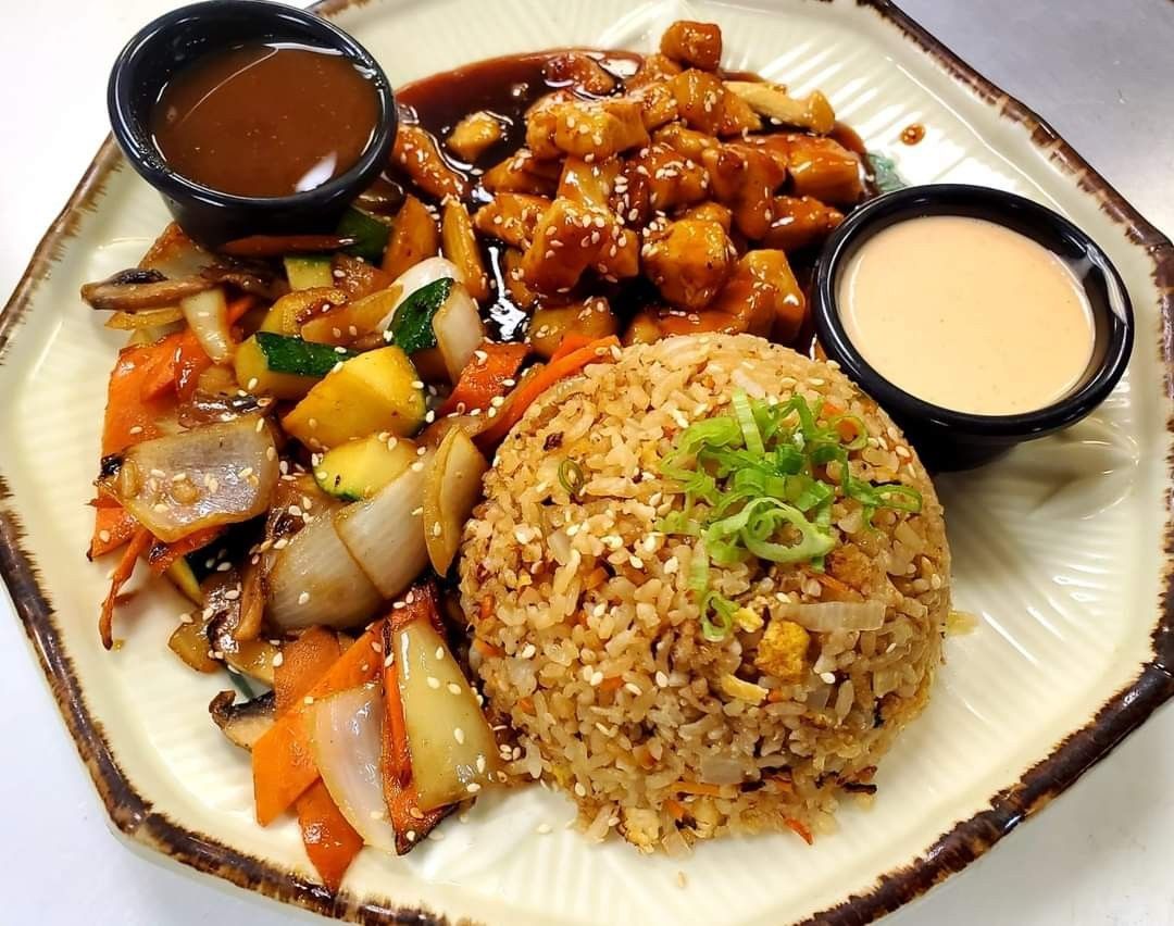Plated fried rice with stir-fried vegetables, sauced chicken, and two dipping sauces
