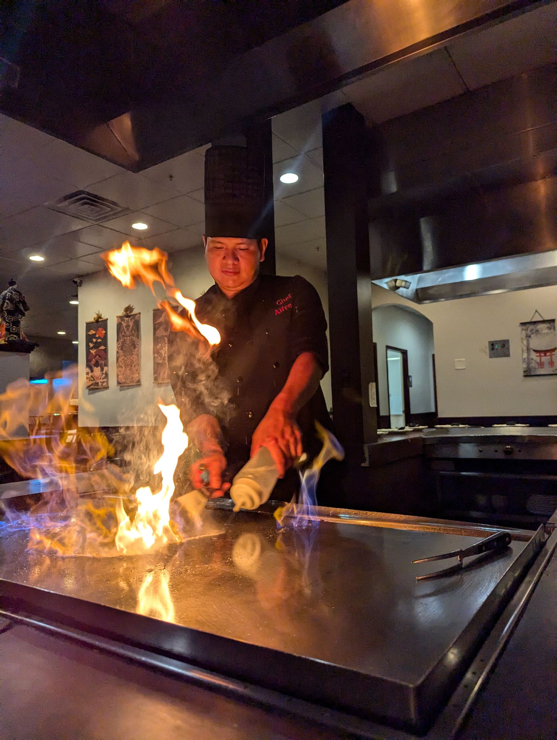 Chef cooking with flames on a flat-top grill in a restaurant kitchen