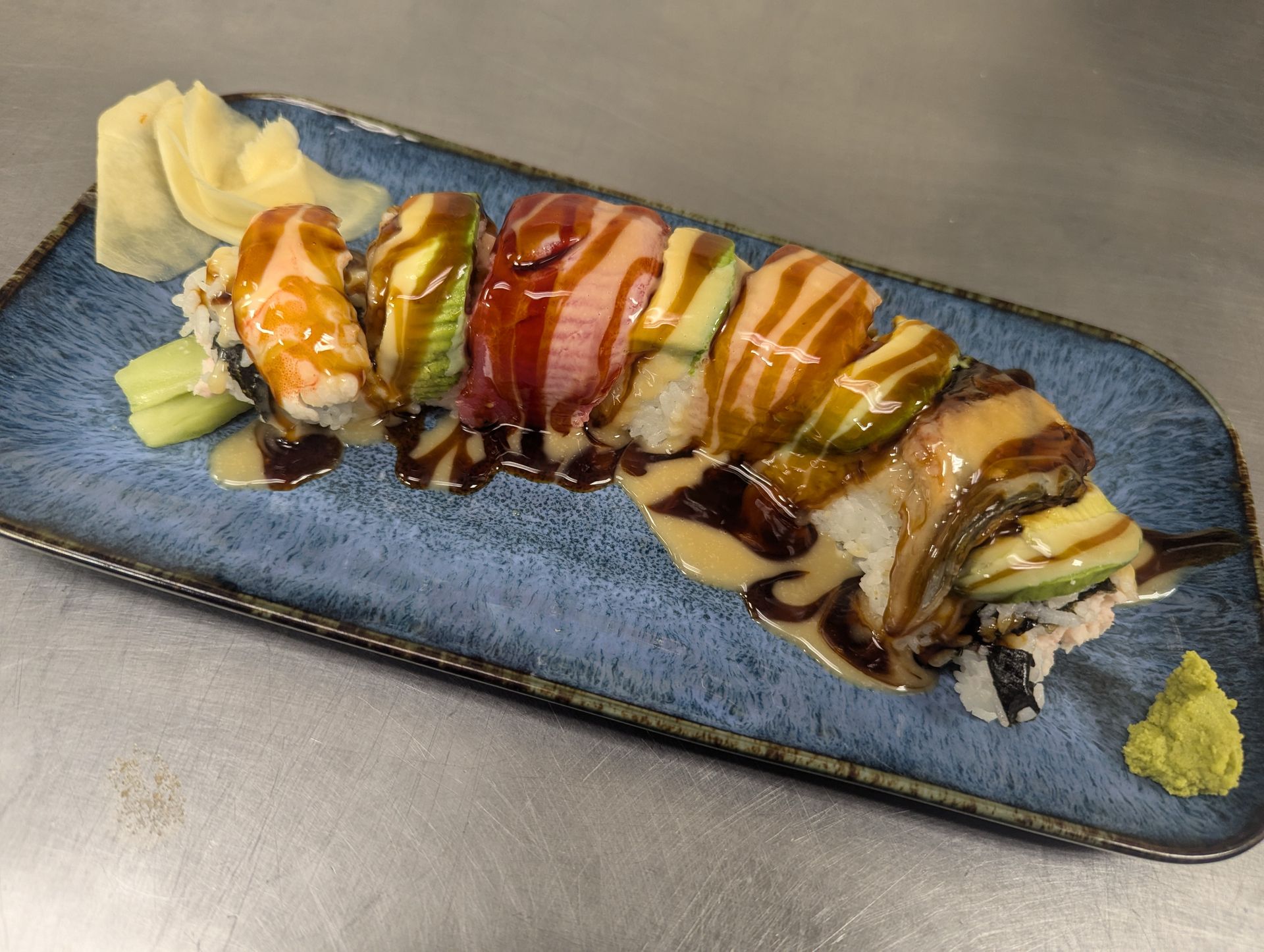 Dessert drizzled with caramel and chocolate on a blue rectangular plate, with whipped cream and fruit garnish