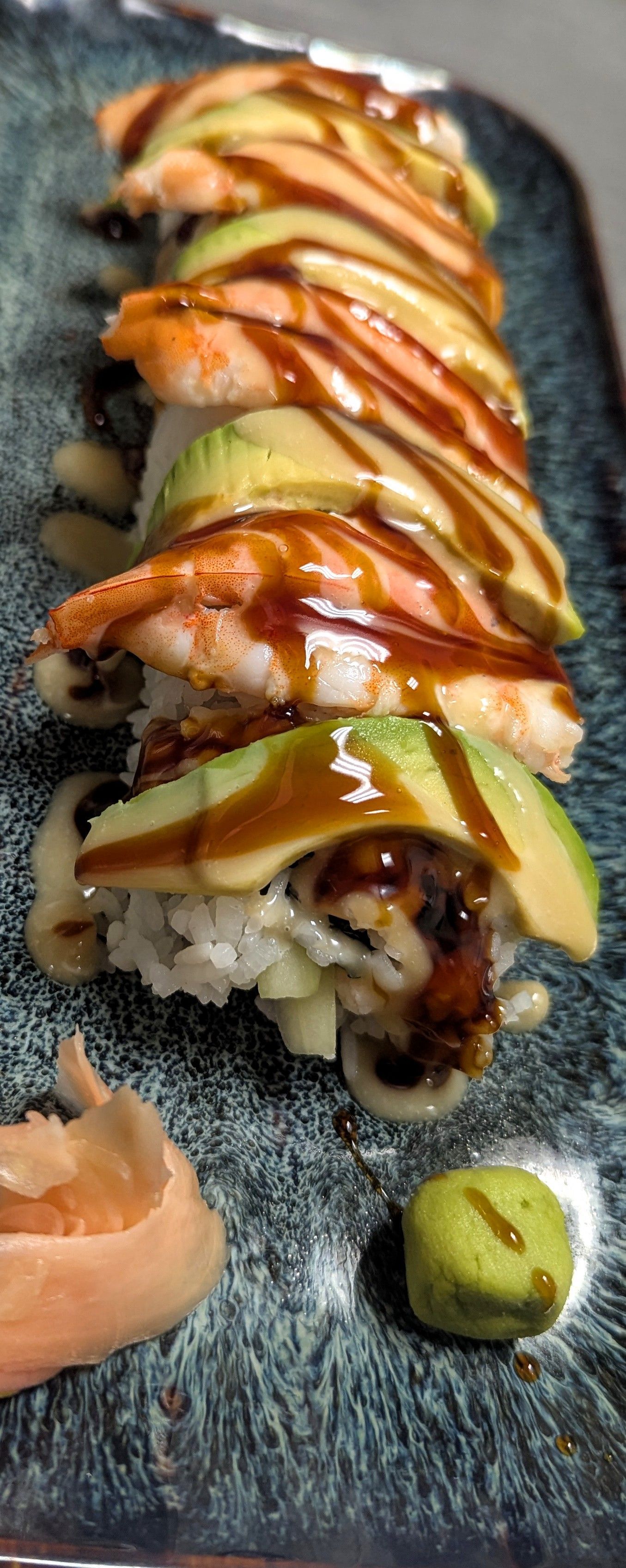 Sushi roll drizzled with sauce and wasabi on a dark plate