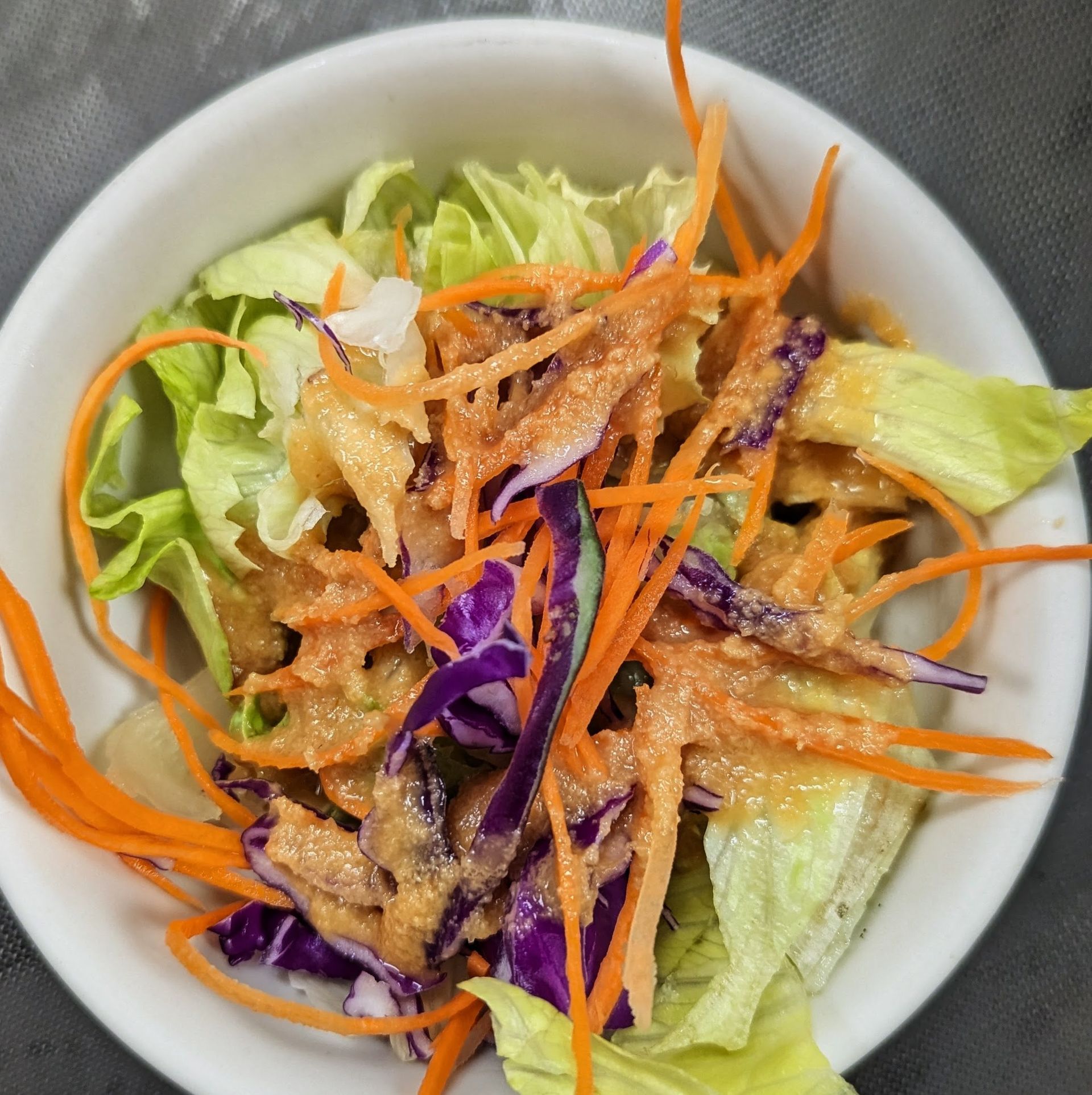 Bowl of salad with lettuce, purple cabbage, shredded carrots, and creamy dressing