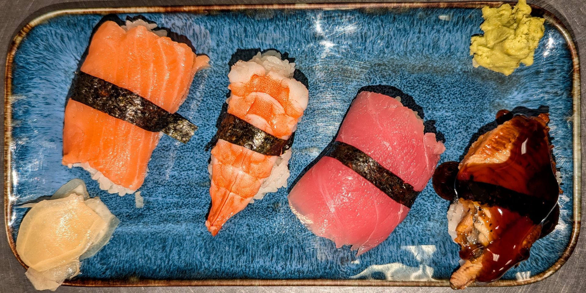 Sushi assortment on a blue tray, including nigiri, wasabi, and ginger.