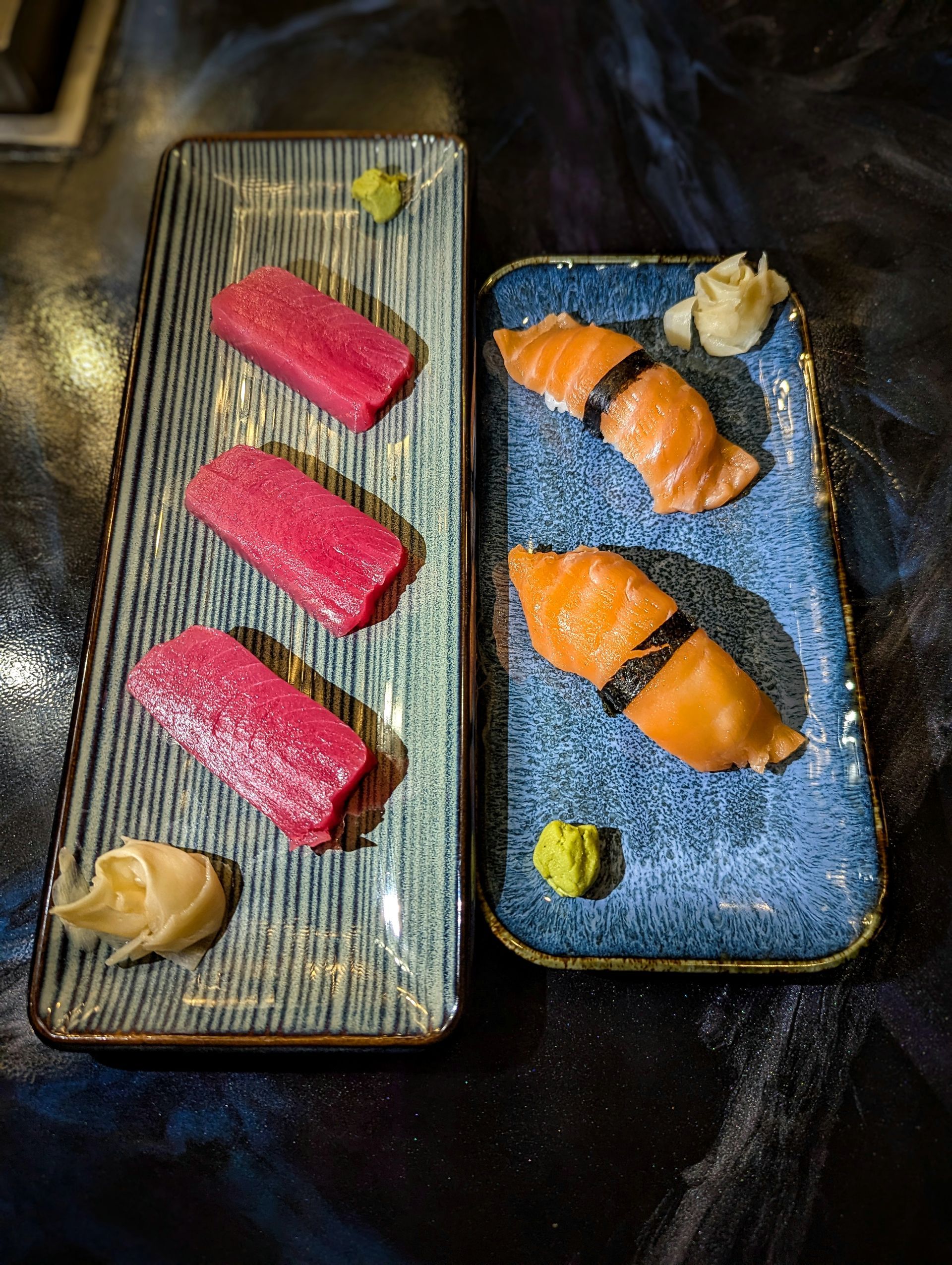 Two sushi plates: pink nigiri on one, salmon nigiri and a garnish on the other.