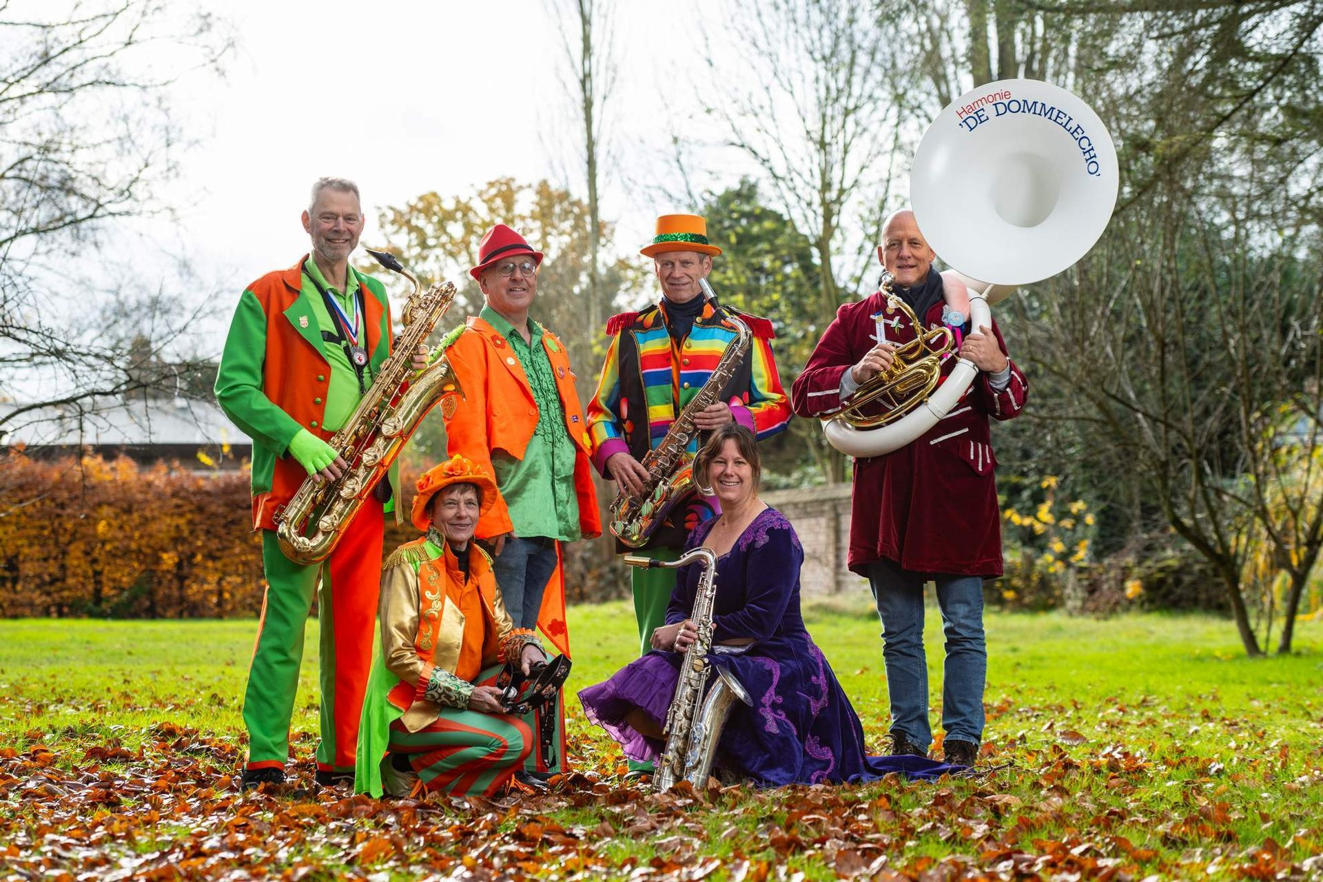 Band in kleurrijke outfits met saxofoons en tuba poseren in een herfstpark.