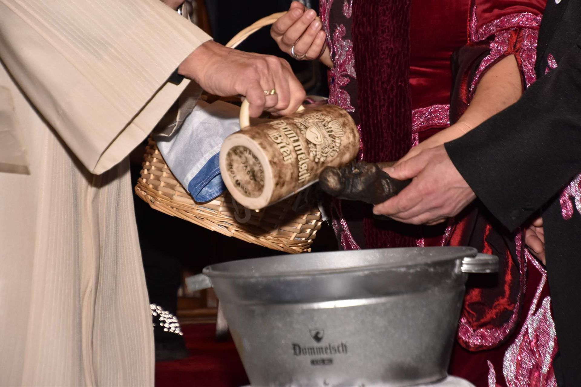 Handen gieten vloeistof uit een houten vat in een metalen bak. Er staat een mandje in de buurt.