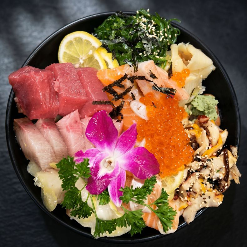Assorted sashimi bowl with salmon, tuna, roe, lemon, seaweed, and orchid garnish