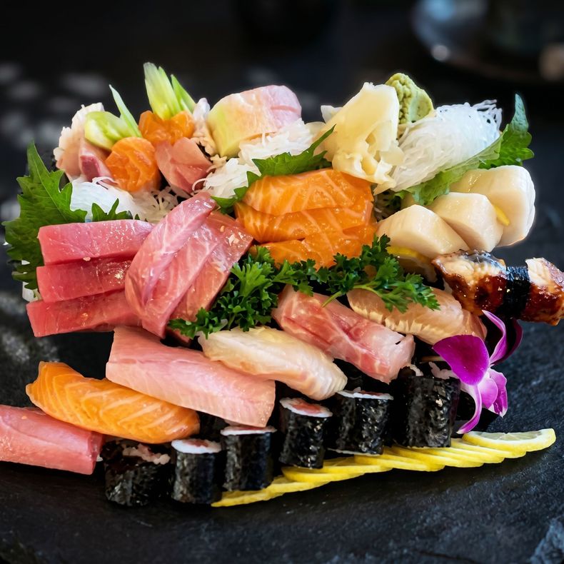 Assorted sushi sashimi platter with salmon, tuna, and garnishes on a black plate