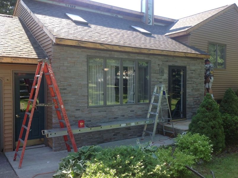 Exterior of a house with construction in progress; brick siding, ladders, and a worker are visible.
