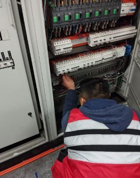 Técnico trabajando dentro de un cuadro de control eléctrico con cableado e interruptores automáticos