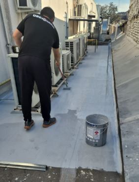 Un trabajador pinta de gris un pasillo en la azotea junto a las unidades de climatización