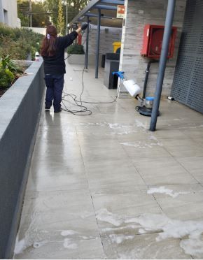 Una persona limpiando con agua a presión un camino de cemento mojado junto a un edificio