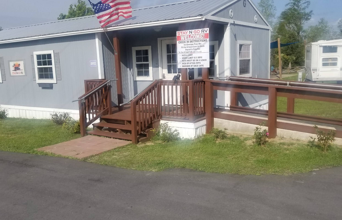 Gray building with brown ramp, stairs, American flag, sign, and grass.