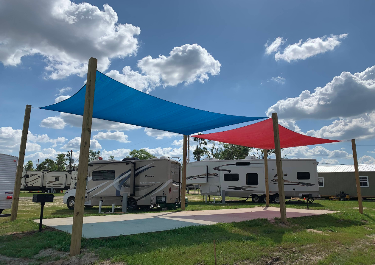 RV campground with blue and red shade sails, sunny day.