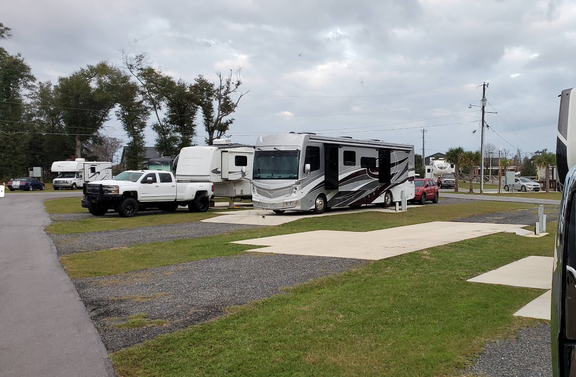 RV campground with motorhomes, pickup trucks, and overcast sky.