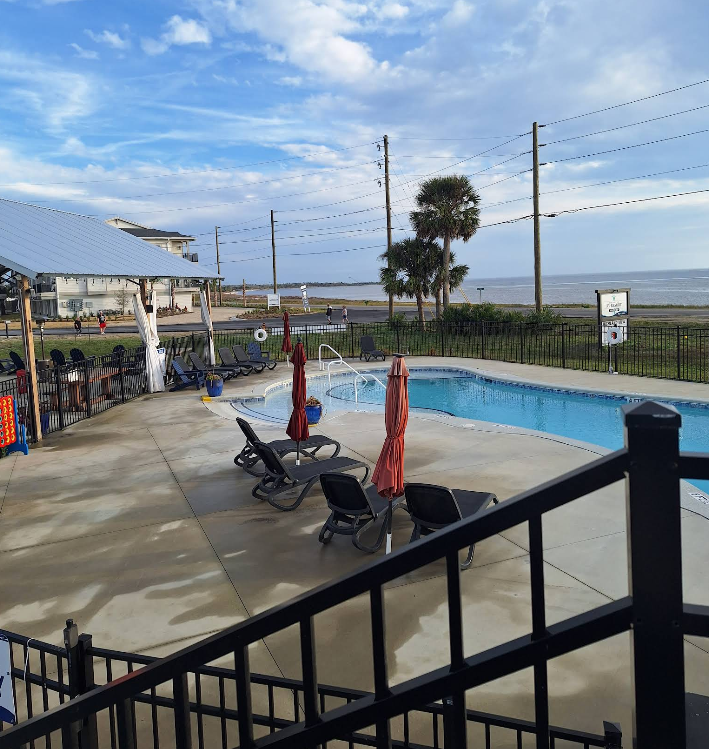 Poolside scene with pool, chairs, umbrellas, and ocean view on a sunny day.