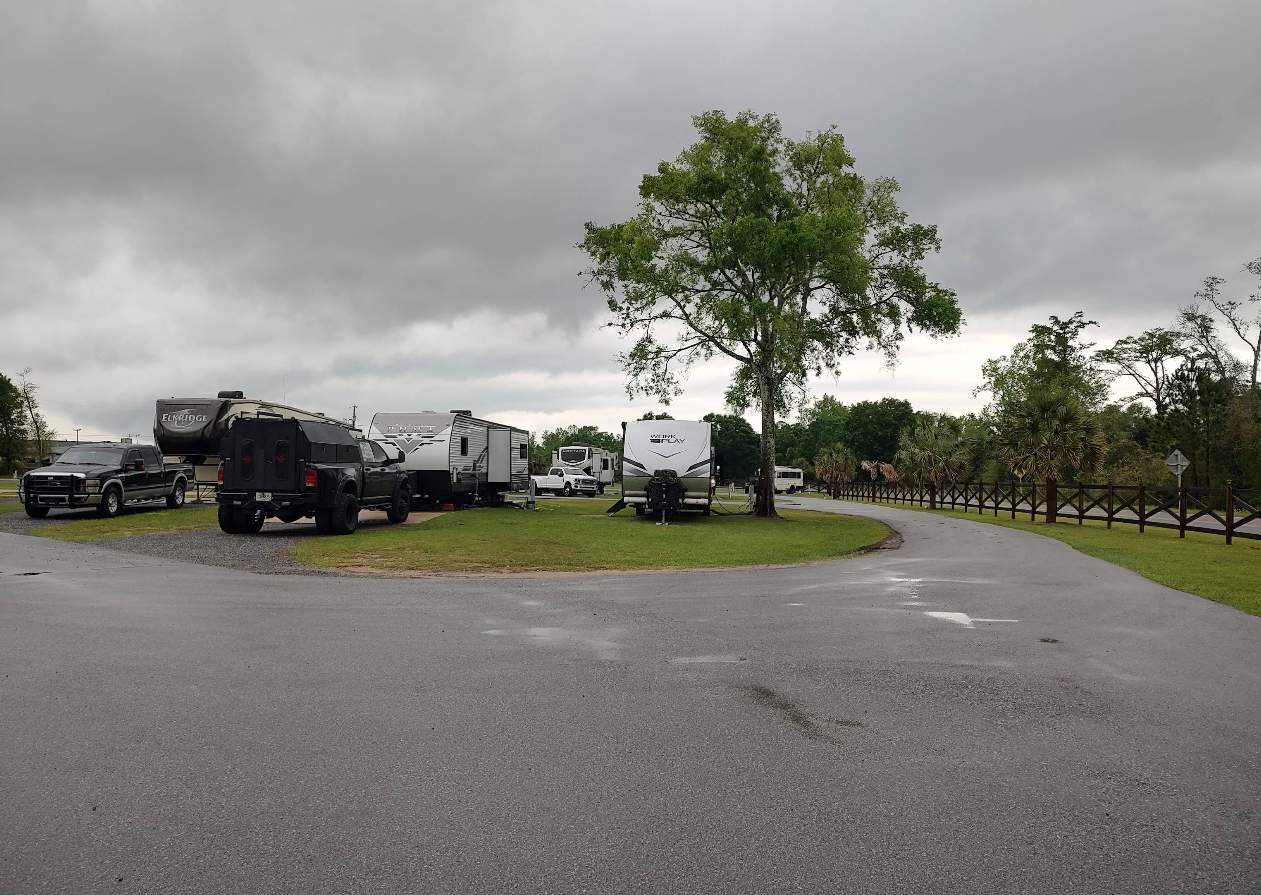 Campground with RVs and trucks parked on grass and pavement, overcast sky.