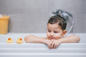Child leaning on bathtub edge with two yellow rubber ducks nearby